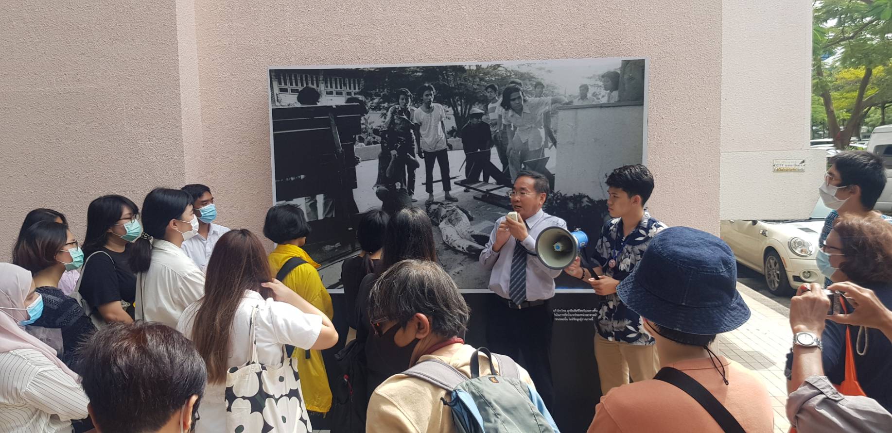 1: 1976년 10월 6일 대학생 데모 사건에 참여했던 당사자(당시 선배 대학생)의 자원으로, 그의 기억과 경험을 공유하는 안내원 역할을 맡았습니다. 피해 사진이 걸린 벽은 희생자들이 총에 맞아 죽은 곳입니다. (사진제공: Patporn (Aor) Phoothong)